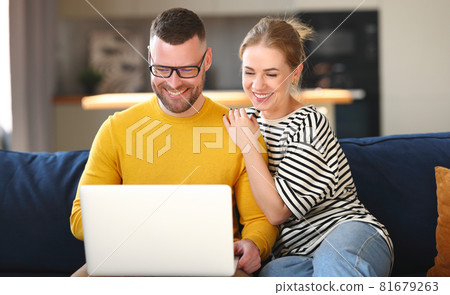 Young happy family couple using laptop while sitting on sofa at home 81679263