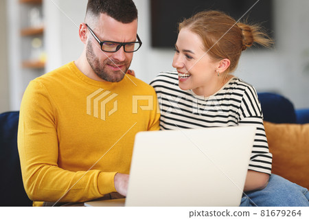 Young happy family couple using laptop while sitting on sofa at home 81679264