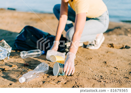 Young female volunteer hand satisfied with picking up trash, a plastic bottles and coffee cups, clean up beach with a sea. Woman collecting garbage. Environmental ecology pollution concept. Earth Day Young female volunteer hand satisfied with picking up trash, a plastic bottles and coffee cups, clean up beach with a sea. Woman collecting garbage. Environmental ecology pollution concept. Earth Day 81679365