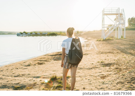 Young Female volunteer with bag and gloves picking up trash, a plastic bottles, clean up beach with a sea. Woman collecting garbage. Environmental ecology pollution concept. Earth Day Young Female volunteer with bag and gloves picking up trash, a plastic bottles, clean up beach with a sea. Woman collecting garbage. Environmental ecology pollution concept. Earth Day 81679366
