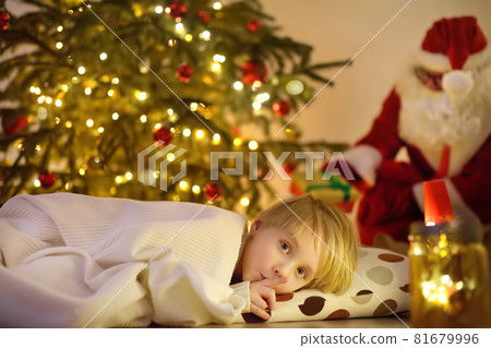 Little boy waiting Santa Claus under tree on Christmas Eve. Santa Claus brought gifts. Child not sleeping, but he does not show it. Magic at Christmas and New Year night. 81679996