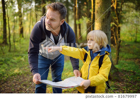 Schoolchild and his mature father hiking together and exploring nature. Little boy with dad looking map during orienteering in forest. Adventure, scouting and hiking tourism for kids. 81679997