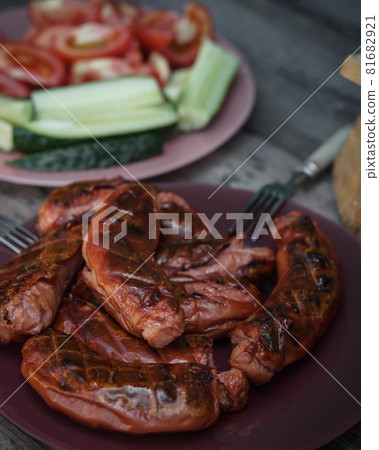 Hot sausages with grill close-up. Serving option with cutting vegetables on a wooden table. Vertical composition 81682921