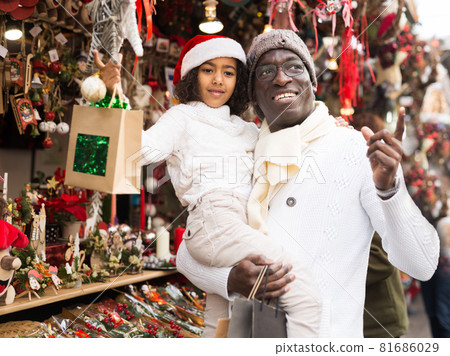 Joyful man holding daughter, pointing to toys at Christmas fair 81686029
