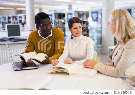 Female tutor helping students preparing for exam in library Female tutor helping students preparing for exam in library 81686068
