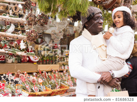 Small girl with father in hat with Christmas toys at fair outdoor Small girl with father in hat with Christmas toys at fair outdoor 81686328