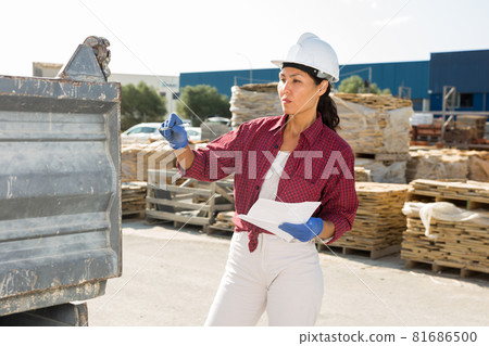 Concentrated asian female manager, keeps records of construction materials in a warehouse Concentrated asian female manager, keeps records of construction materials in a warehouse 81686500