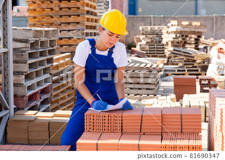 Young female worker writing beside brick stacks 81690347