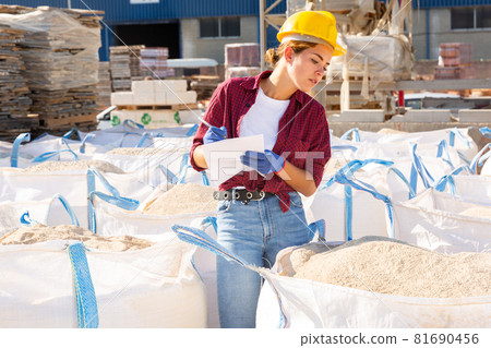 Attentive young female manager keeps records of bulk construction materials in the warehouse Attentive young female manager keeps records of bulk construction materials in the warehouse 81690456