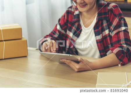 Asian woman startup small business at home office. Online seller entrepreneur young asian woman use tablet checking online order. Woman using tablet check stock goods supply delivery package shipping Asian woman startup small business at home office. Online seller entrepreneur young asian woman use tablet checking online order. Woman using tablet check stock goods supply delivery package shipping 81691040