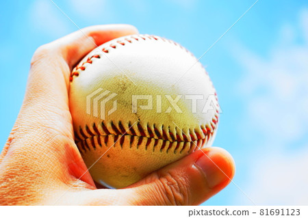 A hand holding a baseball and lifting it up under the blue sky 81691123