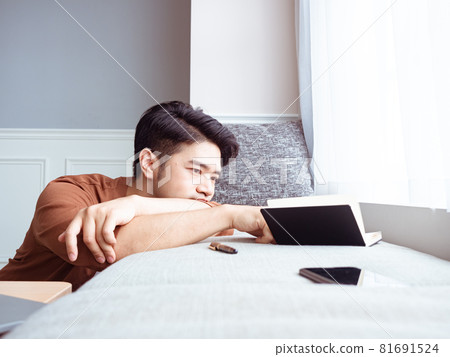 Young Asian man reading book while relaxing at home 81691524
