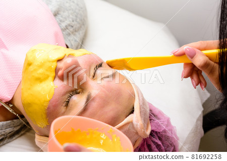 Applying a gold mask on a woman's face, a procedure in a beauty salon. 81692258