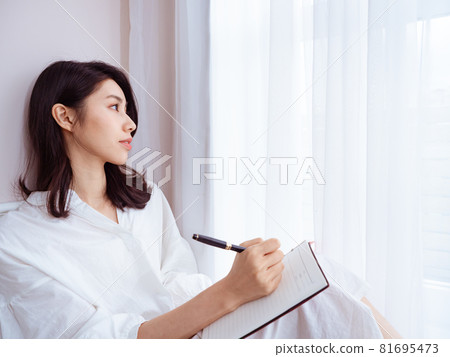 A beautiful young Asian woman writes something in a book A beautiful young Asian woman writes something in a book 81695473