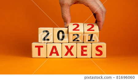 2022 taxes new year symbol. Businessman turns wooden cubes and changes words 'Taxes 2021' to 'Taxes 2022'. Beautiful orange background, copy space. Business, 2022 taxes new year concept. 81696060