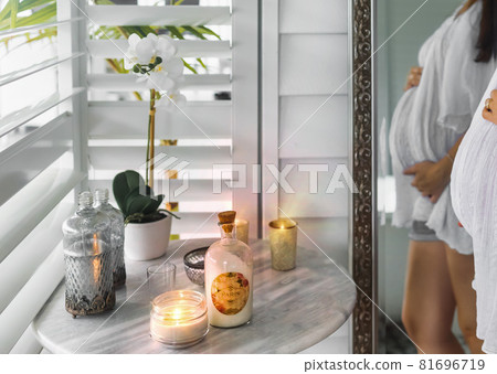 Candles and orchid flowers on the table in bathroom, pregnant belly in the mirror Candles and orchid flowers on the table in bathroom, pregnant belly in the mirror 81696719