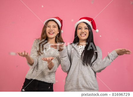 Portrait of a cheerful beautiful Asian womanl wearing dress standing standing under confetti rain and celebrating isolated over pink background 81696729