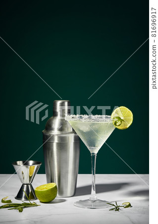 Martini cocktail with ice and slice of lime and shaker on a marble table. An alcoholic cocktail or non-alcoholic mocktail. 81696917