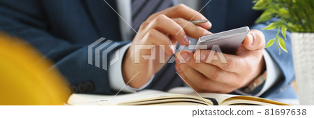 Businessman holds smartphone in his hands and diary is on table 81697638