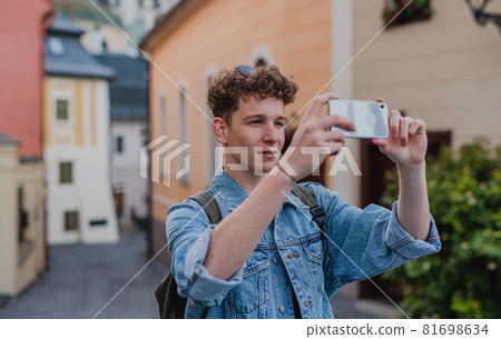 Young man outdoors on trip in town, taking photograph with smartphone. Young man outdoors on trip in town, taking photograph with smartphone. 81698634