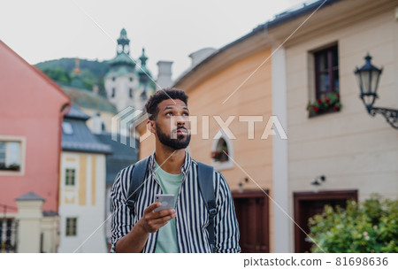 Young man outdoors on trip in town, using online map on smartphone. Young man outdoors on trip in town, using online map on smartphone. 81698636