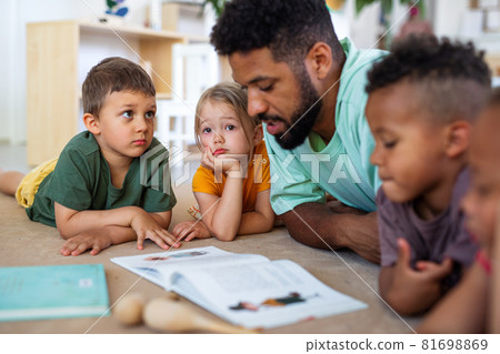 Group of small nursery school children with man teacher on floor indoors in classroom, reading book. Group of small nursery school children with man teacher on floor indoors in classroom, reading book. 81698869