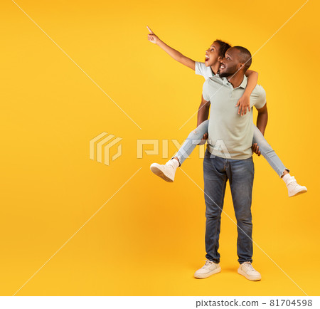 Discounts for family and kids. Excited black man giving piggyback ride for daughter, cute girl pointing at empty space 81704598