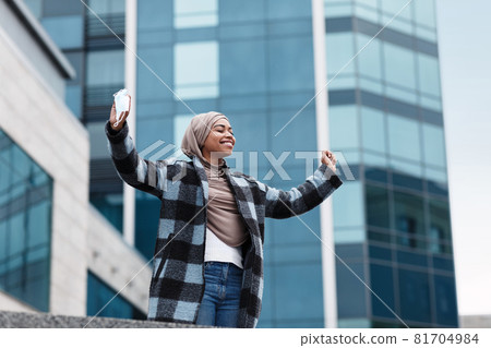 Satisfied happy muslim afro american lady in hijab and coat took off her protective mask and enjoys fresh air in city Satisfied happy muslim afro american lady in hijab and coat took off her protective mask and enjoys fresh air in city 81704984