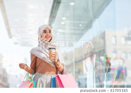 Inspired happy emotional cute millennial middle eastern lady in hijab with many packages and cup of drink Inspired happy emotional cute millennial middle eastern lady in hijab with many packages and cup of drink 81705385
