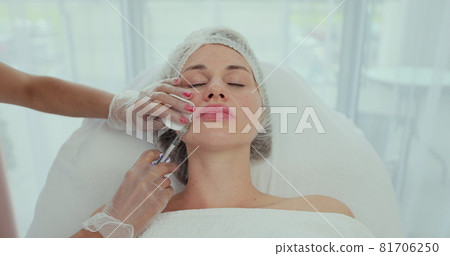 Facial rejuvenation procedure - female doctor injects injections of hyaluronic acid into nasolabial folds to young woman client. 81706250