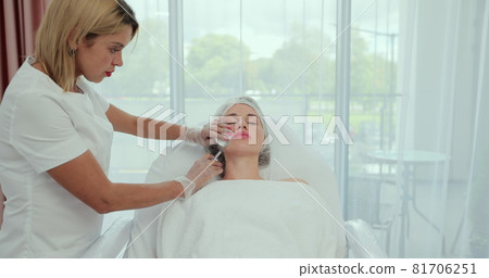 Beautician injects hyaluronic acid into the lips of a girl with a syringe. The cosmetologist doctor performs the procedure in the cosmetology office. 81706251