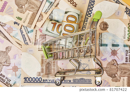 Buying us dollars in Uzbekistan. US dollars roll in shopping trolley and pile of Uzbek sums. Uzbek money and us dollar money exchange 81707422