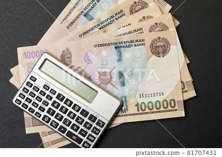 Uzbek money and calculator on black. Pile of Uzbek sums and calculator. Concept of exchange rate. Economic or financial concept Uzbek money and calculator on black. Pile of Uzbek sums and calculator. Concept of exchange rate. Economic or financial concept 81707431