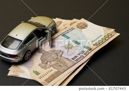 Uzbek sums and car toy. Concept of auto vehicle insuarance in Uzbekistan. Pile of 100000 sums and modern automobile toy on black background. Auto tax, auto insurance, automobile tax concepts Uzbek sums and car toy. Concept of auto vehicle insuarance in Uzbekistan. Pile of 100000 sums and modern automobile toy on black background. Auto tax, auto insurance, automobile tax concepts 81707443