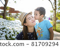 The little son kissed his mother's cheek, who was smiling happily in the beautiful flower garden. 81709294