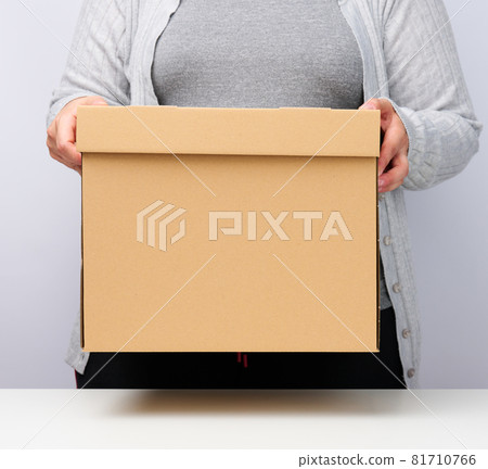 woman in gray clothes stands and holds a brown box on a white background, moving, sending and delivering goods woman in gray clothes stands and holds a brown box on a white background, moving, sending and delivering goods 81710766