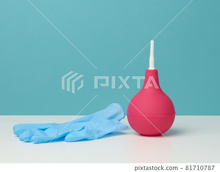 pink rubber enema on white table, medical instrument for cleaning the body, blue background pink rubber enema on white table, medical instrument for cleaning the body, blue background 81710787
