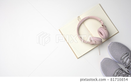 pink wireless headphones, a pair of sneakers and a notepad on a white background, top view. Womens clothing 81710854