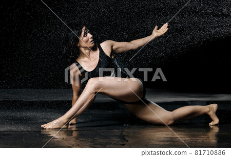 woman with black hair lies on the ground under raindrops on a black background. Woman dressed in black bodysuit 81710886