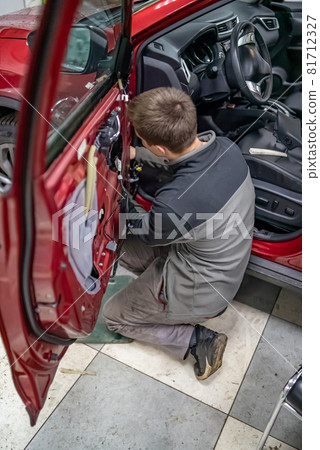 Mechanic guy in automobile service stay on a knees near car door Mechanic guy in automobile service stay on a knees near car door 81712327