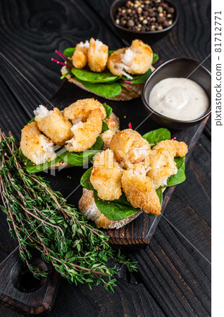 Toasts with Crispy Fried Shrimps Prawns and green salad on a wooden board. Black wooden background. Top view Toasts with Crispy Fried Shrimps Prawns and green salad on a wooden board. Black wooden background. Top view 81712771
