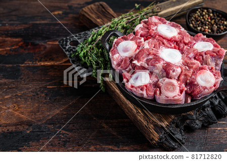 Raw veal beef Oxtail Meat on butcher wooden board with cleaver. Dark wooden background. Top view. Copy space 81712820