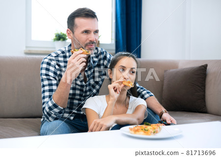Couple watching TV while eating pizza 81713696