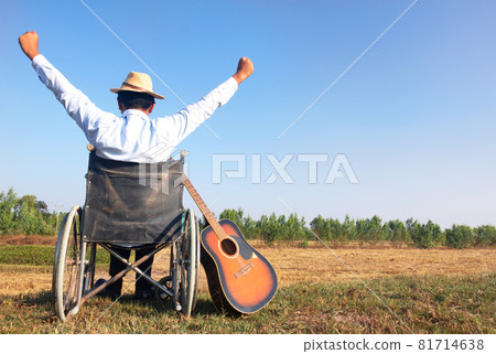 Young disabled man and field background. He is raising guitar and looking into sky.He is wearing a hat and sitting on wheelchair.despair,lonely,hope.Photo concept depression and Patient. Young disabled man and field background. He is raising guitar and looking into sky.He is wearing a hat and sitting on wheelchair.despair,lonely,hope.Photo concept depression and Patient. 81714638