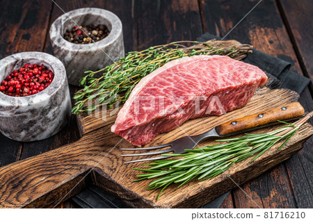 Wagyu A5 raw rump or sirloin steak, kobe beef meat on a butchery board. Dark wooden background. Top view 81716210