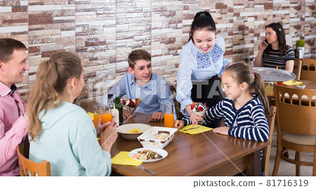 Polite energetic waitress serving dishes to family Polite energetic waitress serving dishes to family 81716319