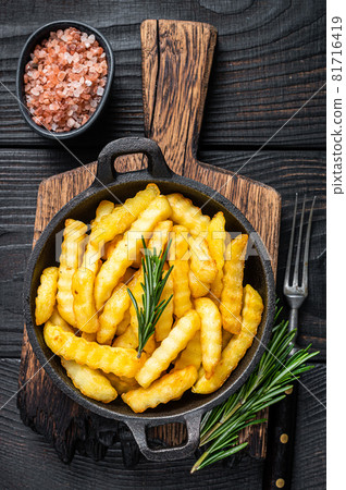 Fried Crinkle French fries potatoes in a pan. Black Wooden background. Top view Fried Crinkle French fries potatoes in a pan. Black Wooden background. Top view 81716419