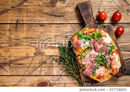 Sliced pizza with prosciutto parma ham, arugula and parmesan cheese on a wooden board. wooden background. Top view. Copy space Sliced pizza with prosciutto parma ham, arugula and parmesan cheese on a wooden board. wooden background. Top view. Copy space 81716601