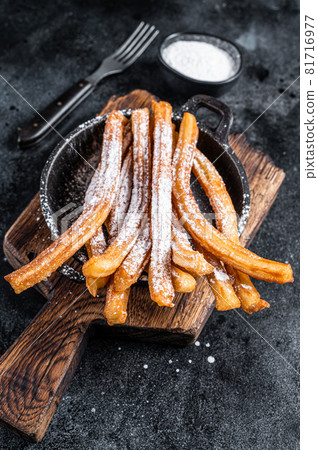Traditional Mexican dessert churros with sugar powder in a pan. Black background. Top view Traditional Mexican dessert churros with sugar powder in a pan. Black background. Top view 81716977