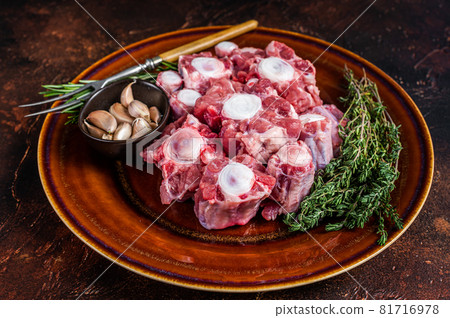 Fresh uncooked beef Oxtail cut Meat on rustic plate with herbs. Dark background. Top view Fresh uncooked beef Oxtail cut Meat on rustic plate with herbs. Dark background. Top view 81716978